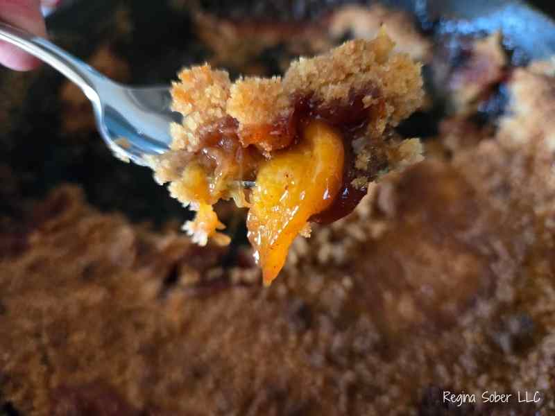 bite of peach cobble with soft peaches and brown crisp cobbler topping.