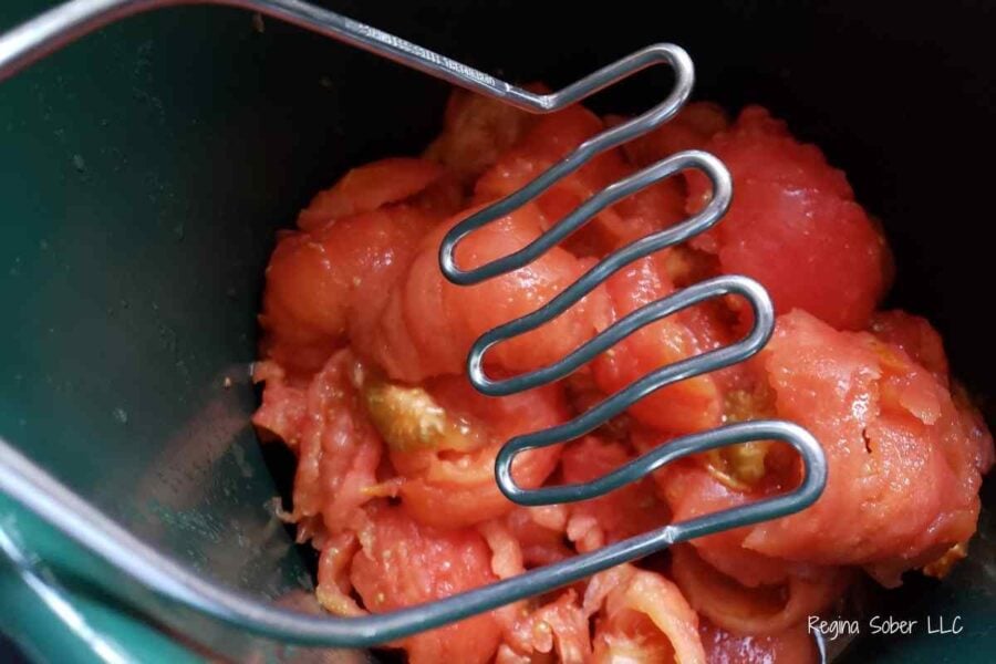 crushing tomatoes with a potato masher