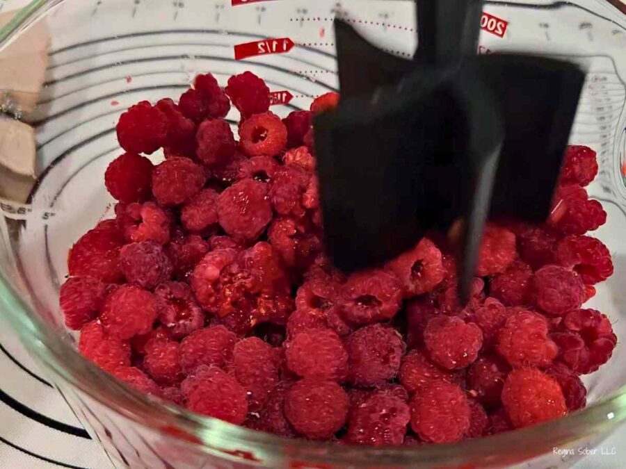 red raspberries being crushed in a glass bowl